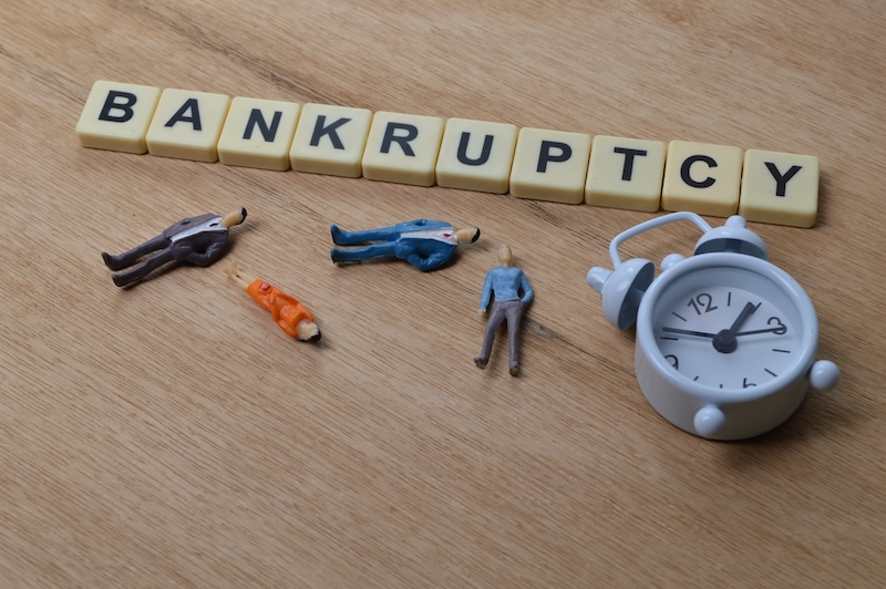 Top angle view of people miniatures, clock and square letters with text BANKRUPTCY.